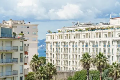 a white building with palm trees in front of the ocean at Studio Velasquez - Welkeys in Cannes