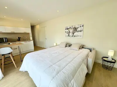 a bedroom with a large white bed and a kitchen at Le studio Palm Beach, Clim ,Parking, Neuf in Cannes