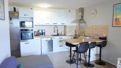 a kitchen with white cabinets and a wooden table with bar stools at Appartement 426, vue mer et piscine by Palmazur in Cannes
