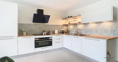 a kitchen with white cabinets and a tv on the wall at Les Genêts - 2 chambres - Terrasse - Climatisé in Le Cannet