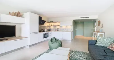 a living room with a couch and a kitchen at Les Genêts - 2 chambres - Terrasse - Climatisé in Le Cannet