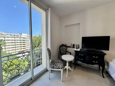 a room with a desk and a television and a balcony at Cannes La Croisette - Joli studio au calme coté jardin in Cannes