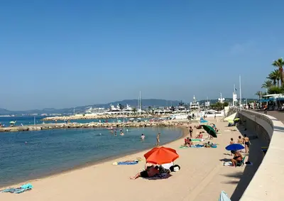 a beach with people laying on the sand and the water at Jardin sur la Pointe Croisette Luxe en Bord de Mer in Cannes