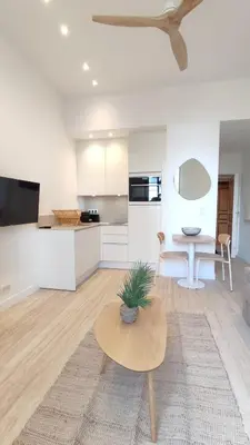 a living room with a table and a kitchen at Studio rénové, vue dégagée et arborée, 700m plage in Cannes