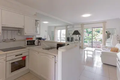 a kitchen with white cabinets and a living room at LE BELLA studio avec balcon idéal pour une évasion à deux, au calme et proche du centre-ville in Cannes