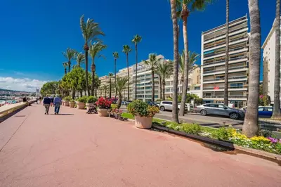 people walking down a sidewalk with palm trees and buildings at Croisette vue mer 2 pièces in Cannes