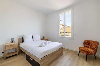 a bedroom with a bed and a chair and a window at LE LOGIS CANNOIS au calme en centre-ville in Cannes