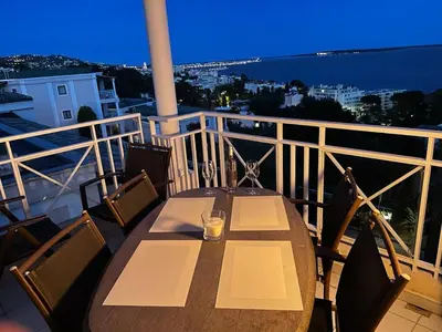 a wooden table and chairs on a balcony at night at Stunning condo with SEA VIEW Balcony & SWIMMING POOL in Cannes