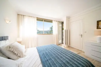 a white bedroom with a bed and a large window at REF 30 - Cannes Croisette - Sea and gardens view apartment for rent in Cannes