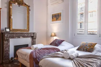 two beds in a room with a mirror and a fireplace at L'Atelier - Jardin, 8mn Palais&Plage, spacieux in Cannes