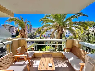 a balcony with chairs and a table and palm trees at LE TRAVOLTA avec merveilleuse terrasse, chic et lumineux à deux pas du centre-ville in Cannes
