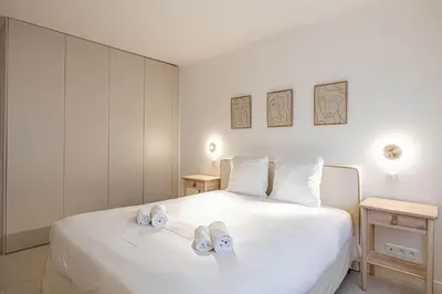 a bedroom with a white bed with slippers on it at LE GRAND BOIS élégant et chaleureux avec balcon, au calme et à deux pas du centre-ville in Cannes