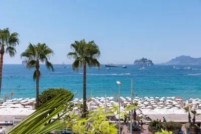 a beach with palm trees and the ocean with umbrellas at 1973 - Luxurious waterfront apartment Croisette in Cannes