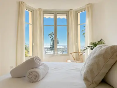 a bedroom with a bed with white sheets and windows at 4A - APARTMENT FACING PORT & Town Hall in Cannes