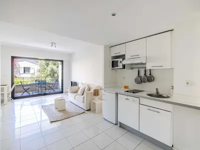 a kitchen with white cabinets and a living room at Charming apt with balcony pool - 1BD 2P - Cannes in Cannes