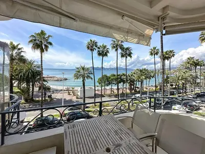 a balcony with a view of the beach and palm trees at Modern 2-Bedroom Stunning Sea View on La Croisette in Cannes
