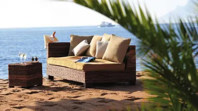 a rattan couch sitting on the beach with the ocean at Residence Aout 12 in Cannes