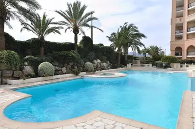 a swimming pool with palm trees and a building at Cannes, La Palme d'Or in Cannes