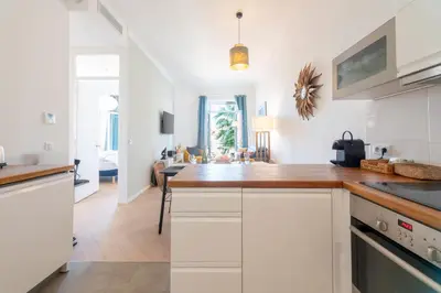 a kitchen with white cabinets and a living room at Modern 2-Br Apartment with Balconies 3 Min from Palais des Festivals in Cannes