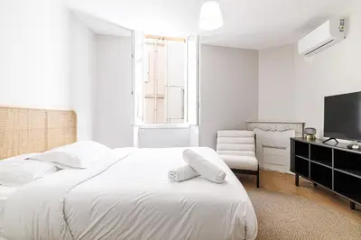 a white bedroom with a large bed and a chair at L'Escapade Cannoise Forville in Cannes