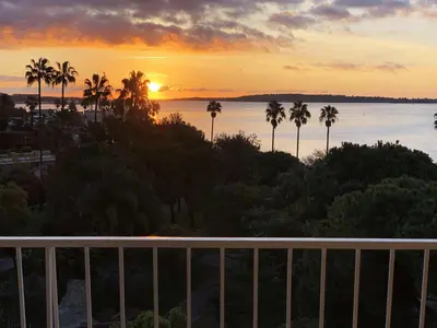 a sunset over the water with palm trees on a balcony at Reflets d'Azur - Vue mer, plage, neuf, moderne in Cannes