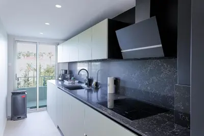 a kitchen with white cabinets and a black counter top at Reflets d'Azur - Vue mer, plage, neuf, moderne in Cannes