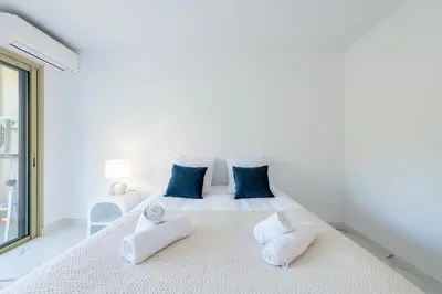 a white bedroom with a large bed with blue pillows at Spacious 2-Br Apartment in a Residence with Pool in Cannes