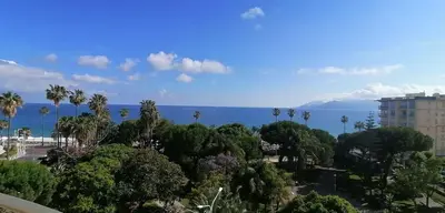 a view of the ocean with palm trees and a building at Cannes centre-ville - Face mer 3 pièces avec terrasse in Cannes