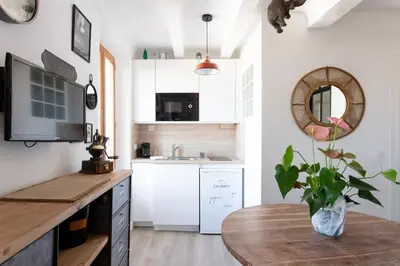 a kitchen with white cabinets and a wooden table at SAVANE -Studio cosy proche Croisette-Classé 2 Etoiles in Cannes
