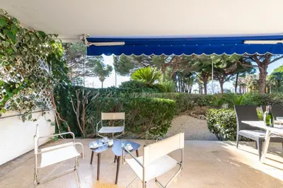 a patio with chairs and a table and a blue umbrella at Garden level Croisette sea view with garage in Cannes
