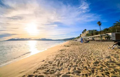 a beach with people sitting on the sand and the ocean at RIO - 200 m plages - App 6pers- climatisé, terrasse, piscine, parking in Cannes