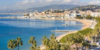 a view of a beach with palm trees and a city at À 1km Plage du Midi et Palais des Festivals - Appartement Centre Cannes avec Cour Extérieur Privée in Cannes
