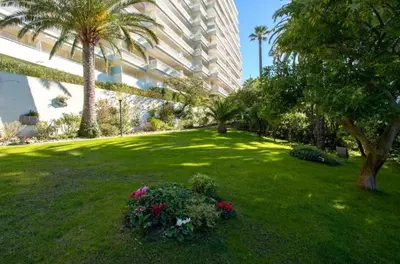 a green yard with palm trees and flowers in front of a building at L'Alexandra - 4 pers - Parking - Aperçu mer in Cannes
