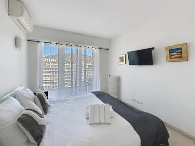 a white bedroom with a large bed and a tv at Beachfront 2-bedroom apartment with balcony in Cannes