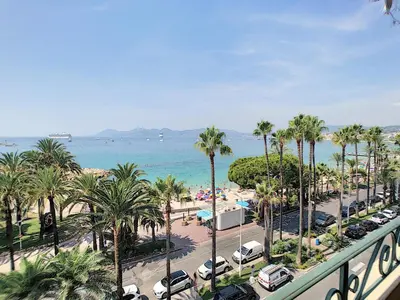 a view of a beach with palm trees and the ocean at 1-bedroom beachfront apartment with sea view in Cannes