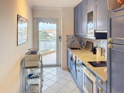 a kitchen with blue cabinets and a large window at A 2 pas des plages du Midi 300L in Cannes