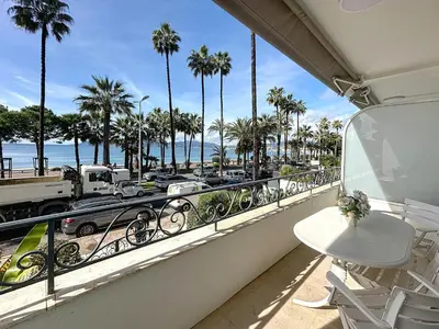 a balcony with a view of the beach and palm trees at 1-bedroom apartment with sea view on La Croisette in Cannes