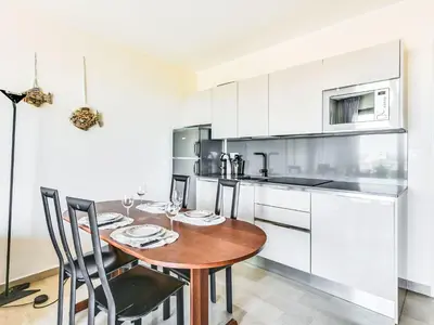 a kitchen with white cabinets and a wooden table and chairs at Apartment Le Katia-2 by Interhome in Cannes