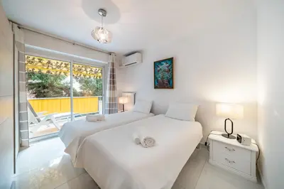 a white bedroom with two beds and a window at 3 pièces au calme avec terrasses et verdure in Cannes