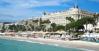 a building on a beach with chairs and umbrellas at Studio Victoria 200 m Carlton Hotel & Croisette in Cannes