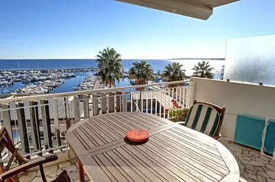 a wooden table on a balcony with a view of a harbor at Henri Camille Agency - Le Cap - 2 bedrooms Apt sea view in Cannes