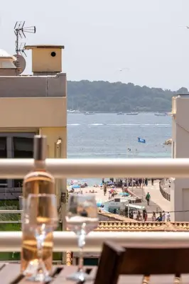 a bottle of wine sitting on a balcony overlooking a beach at Évasion Pointe Croisette, vue mer, plage à une minute in Cannes