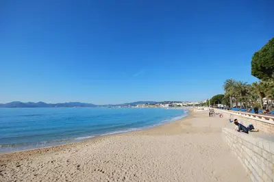a beach with people sitting on the sand and the water at One bedroom apartment Palm Beach in Cannes