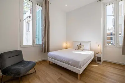 a bedroom with a bed and a chair and two windows at LE COSY un havre de paix près de la Croisette in Cannes