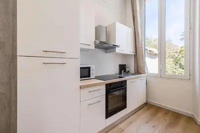 a white kitchen with white cabinets and a window at LE COSY un havre de paix près de la Croisette in Cannes
