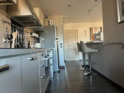 a kitchen with white cabinets and a bar stool at Apartment in park with pool in Cannes