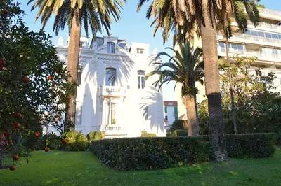 a white house with palm trees in front of a building at Charming Apartment Cannes City Center and Beaches in Cannes