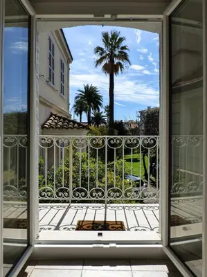 a view from a window of a balcony with a palm tree at Villa Divona - central gem with sunset balcony & pool in Cannes