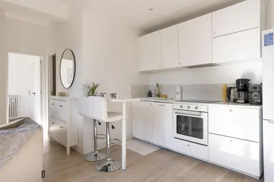 a white kitchen with white cabinets and a table at Astéria - cosy, moderne, clim, 15mn Palais&Plages in Cannes