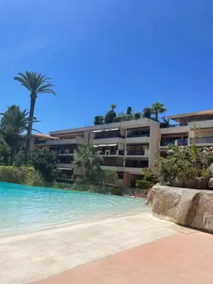 a swimming pool in front of a building with palm trees at Appt 2ch 90m2 avec terrasse 40m2, piscine et tennis in Cannes